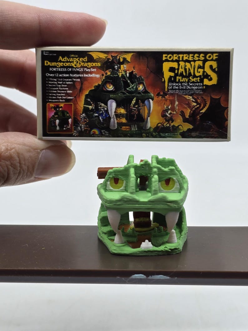 May include: A green plastic Dungeons & Dragons Fortress of Fangs playset with a dragon head design. The box art features a green dragon with fangs and a dungeon interior. The text on the box reads "Official Advanced Dungeons & Dragons Fortress of Fangs Play Set" and "Unlock the Secrets of the Evil Dungeon".