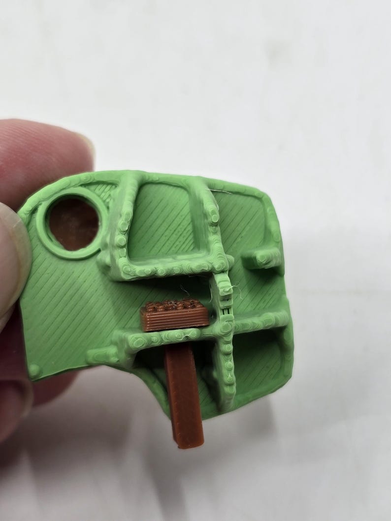 May include: A green 3D printed plastic part with a brown plastic piece inserted into it.
