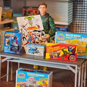 May include: A collection of vintage comic book collector's items, including a Marvel Comic Book Collector's Kit box, a Hall of Justice box, a Super Powers box, and a Tower of Darkness box. The boxes are all brightly coloured and feature iconic comic book characters.