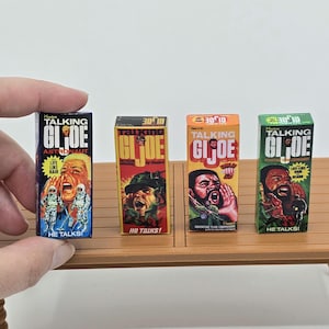 May include: Four vintage G.I. Joe action figure boxes. The boxes are rectangular and feature colorful illustrations of the characters. The boxes are labeled "Talking G.I. Joe" and include the text "He Talks!"