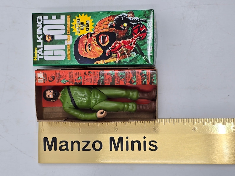Puede incluir: Una figura de acci&oacute;n vintage Hasbro Talking GI Joe en una caja verde y roja. La figura lleva un uniforme verde y tiene barba marr&oacute;n. La caja dice "&iexcl;Habla!" y "Pelo y barba realistas".