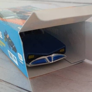 K&ouml;nnte beinhalten: Ein blaues Spielzeugauto mit einem wei&szlig;en und blauen K&uuml;hlergrill und einem blauen und wei&szlig;en Innenraum. Das Auto befindet sich in einer Schachtel mit dem Wort "remarkable" auf der Seite.