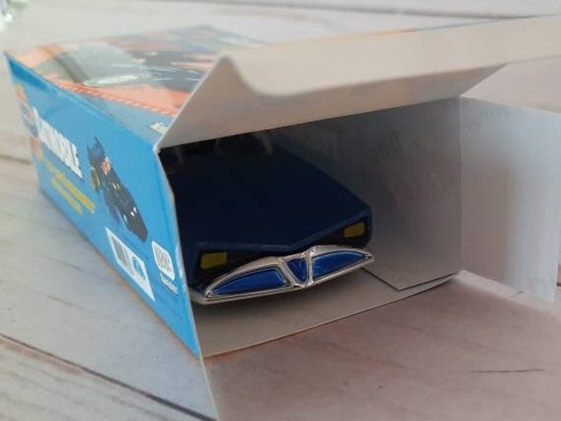 K&ouml;nnte beinhalten: Ein blaues Spielzeugauto mit einem wei&szlig;en und blauen K&uuml;hlergrill und einem blauen und wei&szlig;en Innenraum. Das Auto befindet sich in einer Schachtel mit dem Wort "remarkable" auf der Seite.