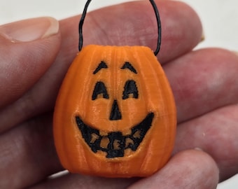 May include: A small orange pumpkin-shaped Halloween trick-or-treat bucket with a black handle and a smiling jack-o'-lantern face.