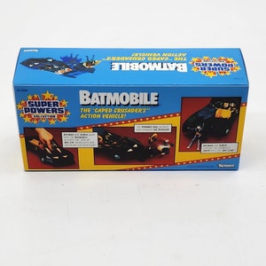 K&ouml;nnte beinhalten: Eine blaue und gelbe Schachtel mit einem schwarzen und grauen Spielzeug-Batmobil darin. Die Schachtel zeigt den Text "Super Powers Collection" und "Batmobile: Das Actionfahrzeug des "Caped Crusader"!" mit einem roten Sternendesign. Das Spielzeug-Batmobil hat einen schwarzen K&ouml;rper mit einer grauen Windschutzscheibe und einem roten Fledermaus-Symbol auf der Motorhaube.