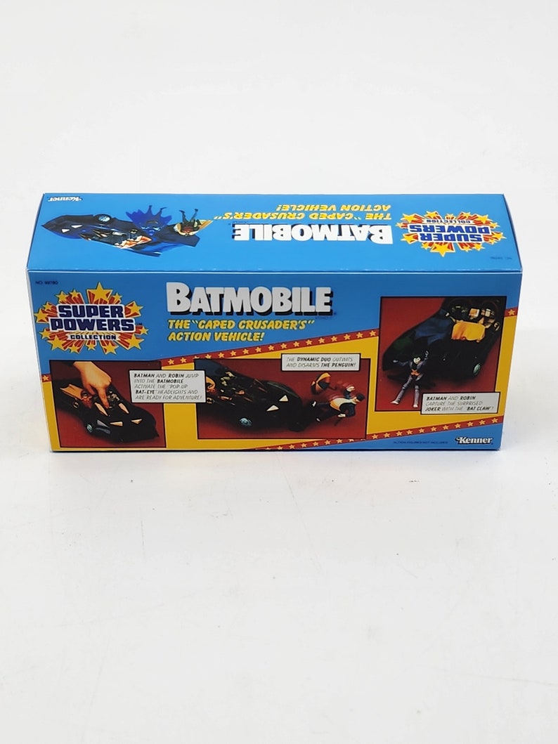 K&ouml;nnte beinhalten: Eine blaue und gelbe Schachtel mit einem schwarzen und grauen Spielzeug-Batmobil darin. Die Schachtel zeigt den Text "Super Powers Collection" und "Batmobile: Das Actionfahrzeug des "Caped Crusader"!" mit einem roten Sternendesign. Das Spielzeug-Batmobil hat einen schwarzen K&ouml;rper mit einer grauen Windschutzscheibe und einem roten Fledermaus-Symbol auf der Motorhaube.