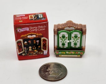 May include: A red box with a picture of a wooden cabinet with doors that open. The box says "Strawberry Shortcake Berry Patch Carry Case". The cabinet is a small plastic toy with green doors and a floral design.