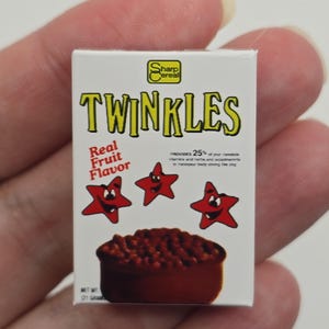 May include: A miniature cereal box for "Twinkles" with a white background and yellow and red text. The box features cartoon star characters and a bowl of cereal. The box reads "Real Fruit Flavor" and "NET WT (21 GRAMS)."