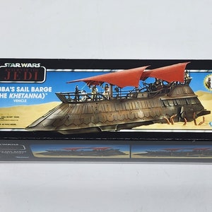 May include: A box for a Star Wars Return of the Jedi Jabba's Sail Barge (The Khetanna) vehicle toy. The box features a colourful illustration of the sail barge on a desert background. The box is black with red and white accents.