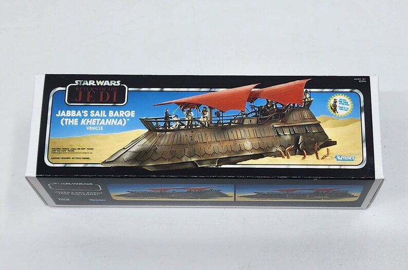 May include: A box for a Star Wars Return of the Jedi Jabba's Sail Barge (The Khetanna) vehicle toy. The box features a colourful illustration of the sail barge on a desert background. The box is black with red and white accents.
