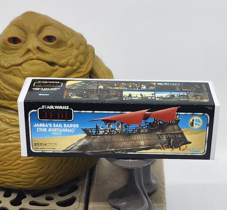 May include: A Star Wars Return of the Jedi Jabba's Sail Barge (The Khetanna) vehicle box. The box is white with blue and red accents. The box features a detailed illustration of the sail barge with Jabba the Hutt's palace in the background. The box also includes the text "Star Wars Return of the Jedi" and "Jabba's Sail Barge (The Khetanna)".