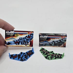 May include: Two G.I. Joe Cobra Command Attack Glider toys. One is blue with black camouflage, and the other is green with black camouflage. The packaging features the G.I. Joe logo and images of the gliders.