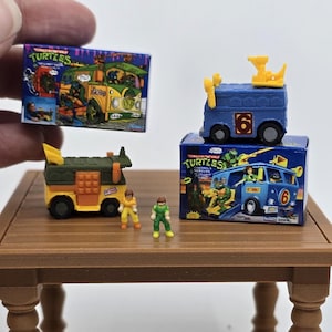 Könnte beinhalten: Miniatur-Spielzeugfahrzeuge und Figuren der Teenage Mutant Ninja Turtles. Das Set enthält einen grünen und gelben Van, einen blauen Van, zwei Actionfiguren und zwei Kartons mit dem Turtles-Logo und Van-Illustrationen.