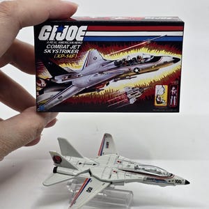 May include: A G.I. Joe Combat Jet Skystriker (XP-14F) toy. The white and gray jet has red and blue accents, with the number 100 on the wings and tail. The box features the G.I. Joe logo and an image of the jet.