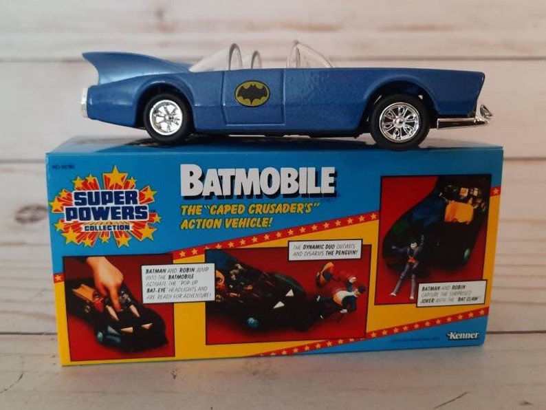 K&ouml;nnte beinhalten: Ein blaues Spielzeug-Batmobil mit den Worten "Super Powers Collection" und "Batmobile The Caped Crusader's Action Vehicle!" auf der Schachtel. Die Schachtel zeigt auch Batman und Robin im Batmobil.