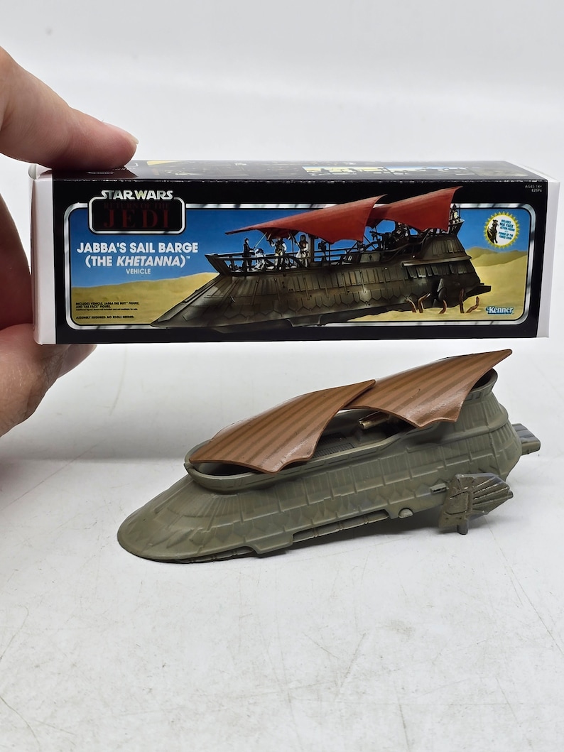 May include: A Star Wars: The Jedi toy sail barge, Jabba's Sail Barge (The Khetanna), in a grey and brown colour scheme. The sail barge is a vehicle from the Star Wars universe. The box is also shown in the image.