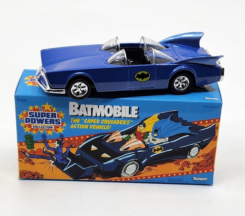 K&ouml;nnte beinhalten: Ein blaues Spielzeug-Batmobil in seiner Originalverpackung. Die Schachtel zeigt Illustrationen von Batman, Robin und dem Joker. Der Text auf der Schachtel lautet "Batmobile", "Das "Kapuzenkreuzfahrers" Actionfahrzeug!" und "Super Powers Collection".