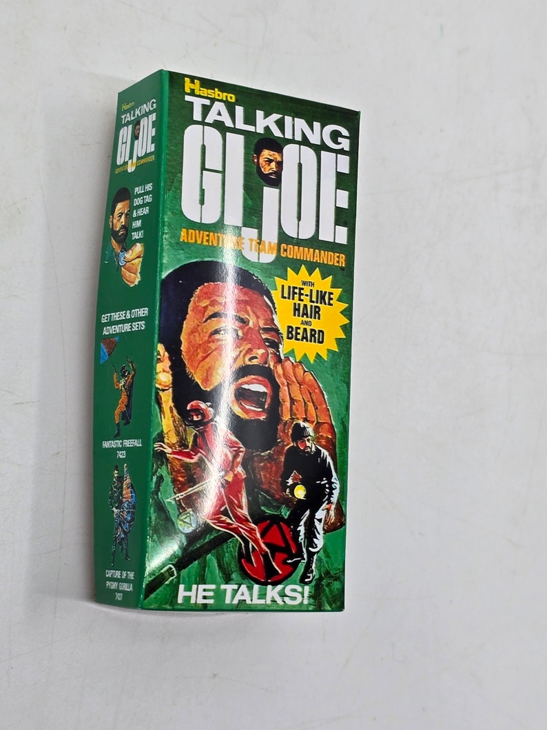 Puede incluir: Una caja verde y amarilla con una imagen de un hombre con barba y un uniforme militar verde. La caja dice "Talking G.I. Joe Adventure Team Commander" y "He Talks!" con una imagen de una placa de identificaci&oacute;n. La caja tambi&eacute;n dice "With Life-Like Hair and Beard".