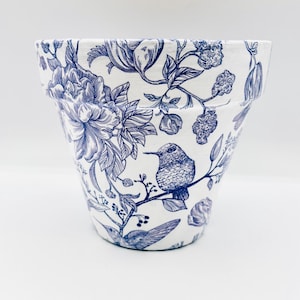 May include: White ceramic flower pot with a blue floral and hummingbird design. The pot features detailed illustrations of flowers, leaves, and a hummingbird perched on a branch. The design is in a classic blue and white color scheme.