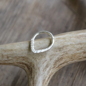 Puede incluir: Un anillo de plata con un diseño texturizado en forma de lágrima. El anillo está apoyado en una pieza de asta.