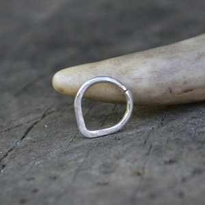 Puede incluir: Un anillo de plata con forma de lágrima. El anillo está sobre una superficie de madera.