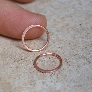 Può includere: Due orecchini a cerchio in oro rosa, uno più grande dell'altro, su una superficie marrone chiaro.