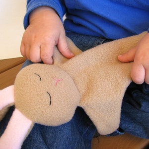 May include: A child holds a brown plush bunny with pink ears and embroidered eyes. The bunny is lying on the child's lap.