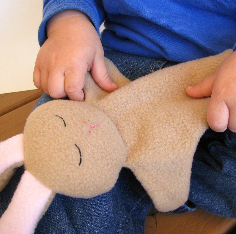 May include: A child holds a brown plush bunny with pink ears and embroidered eyes. The bunny is lying on the child's lap.