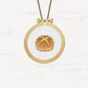 May include: A brown and tan cross-stitch embroidery of a bun, in a wooden embroidery hoop.