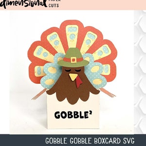 May include: A papercraft turkey box card with a red, yellow, and blue patterned tail, a brown head, a green hat with a gold buckle, and the word "GOBBLE" on the front.