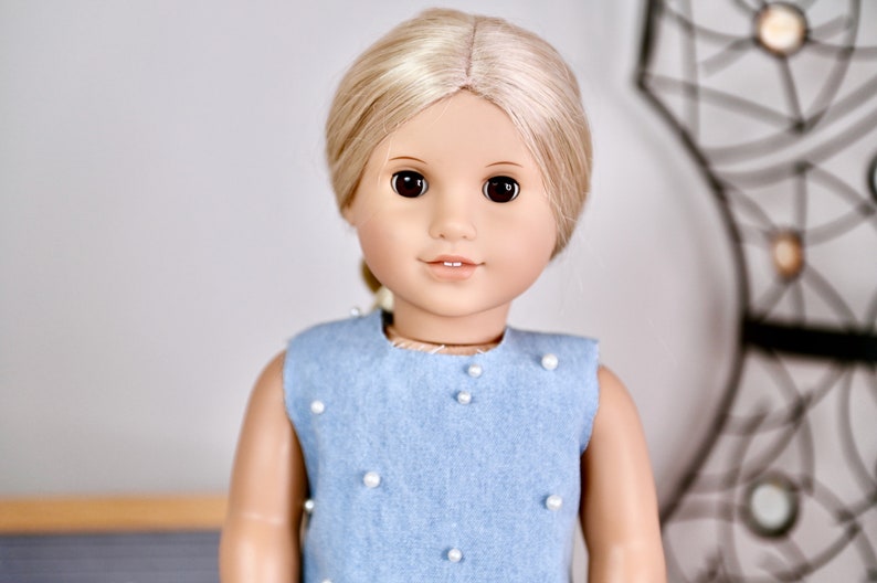 May include: A doll with blonde hair wearing a light blue sleeveless dress with white pearl embellishments.