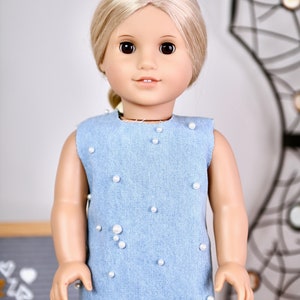 May include: A light blue denim dress with white pearl embellishments. The dress is sleeveless and has a round neckline.