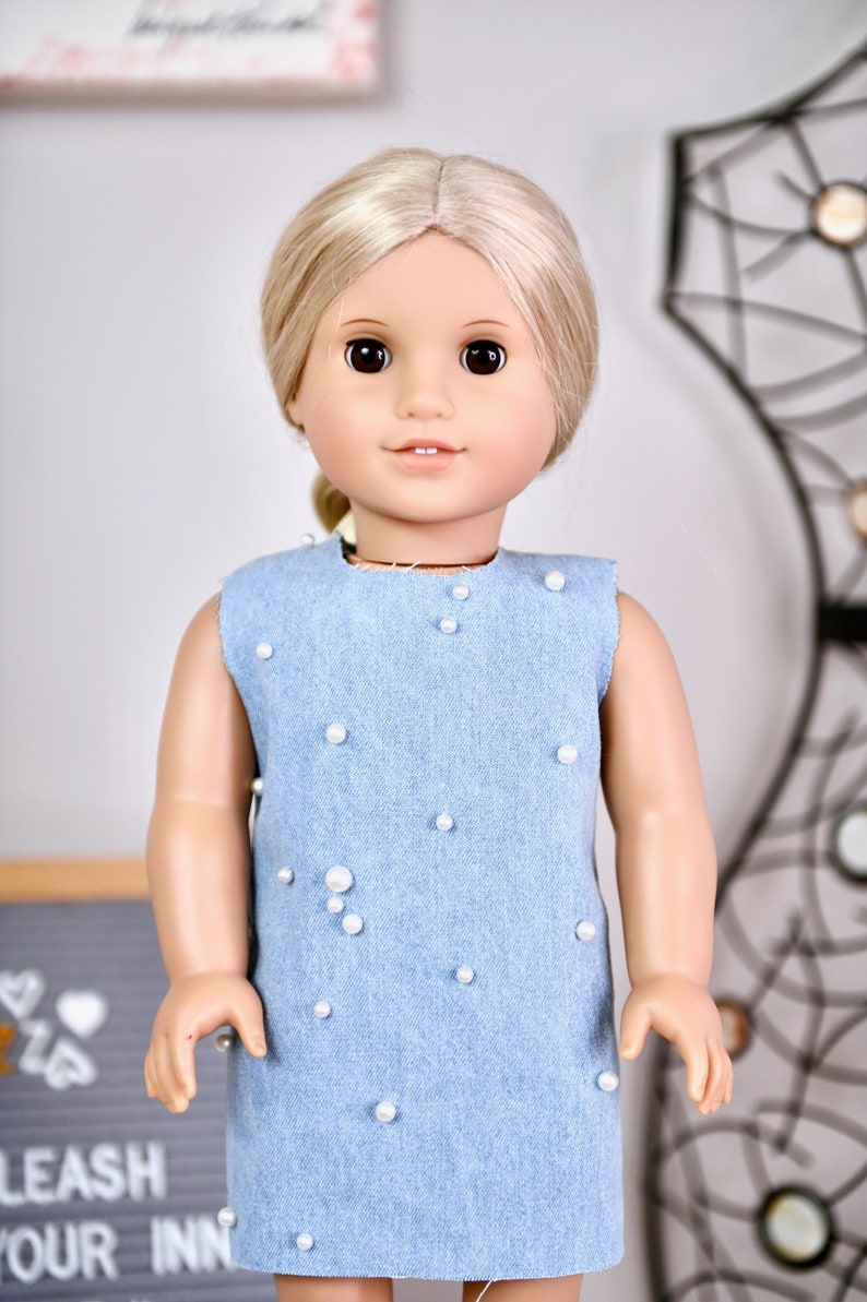 May include: A light blue denim dress with white pearl embellishments. The dress is sleeveless and has a round neckline.