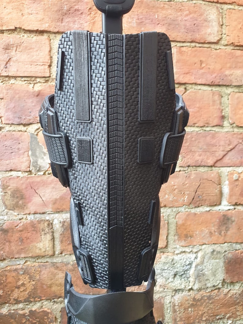 May include: Black knee brace with a textured, woven design and adjustable straps. The brace has a rigid, supportive structure.