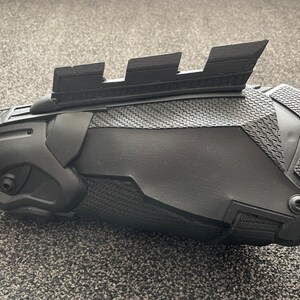 May include: A black 3D printed forearm brace with a textured surface and a series of raised ridges on the top.