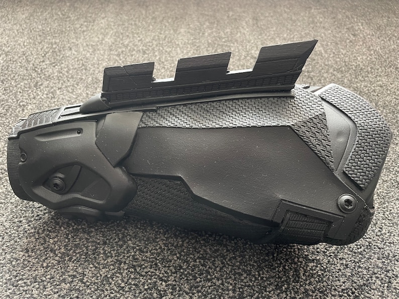 May include: A black 3D printed forearm brace with a textured surface and a series of raised ridges on the top.
