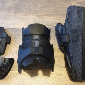 May include: Four black knee pads with a textured surface and straps. The knee pads are designed for protection and support.