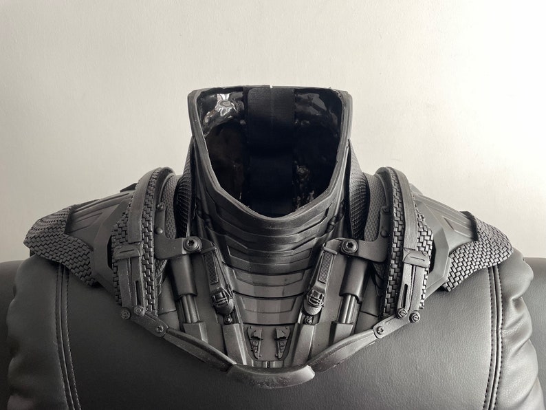 May include: Black and gray futuristic-style costume neck piece with a textured surface and multiple straps and buckles.
