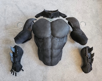 May include: Black fabric costume pieces for a superhero costume. The pieces include a chest plate, two arm pieces, two forearm pieces, and a neck piece.