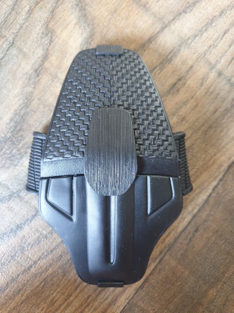 May include: Black leather holster with a textured surface and a strap. The holster has a raised section on the top for a belt clip.