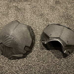 May include: Two black, textured, helmet-like pieces, possibly for cosplay or costume use. The pieces are made of a material that resembles molded plastic or rubber.