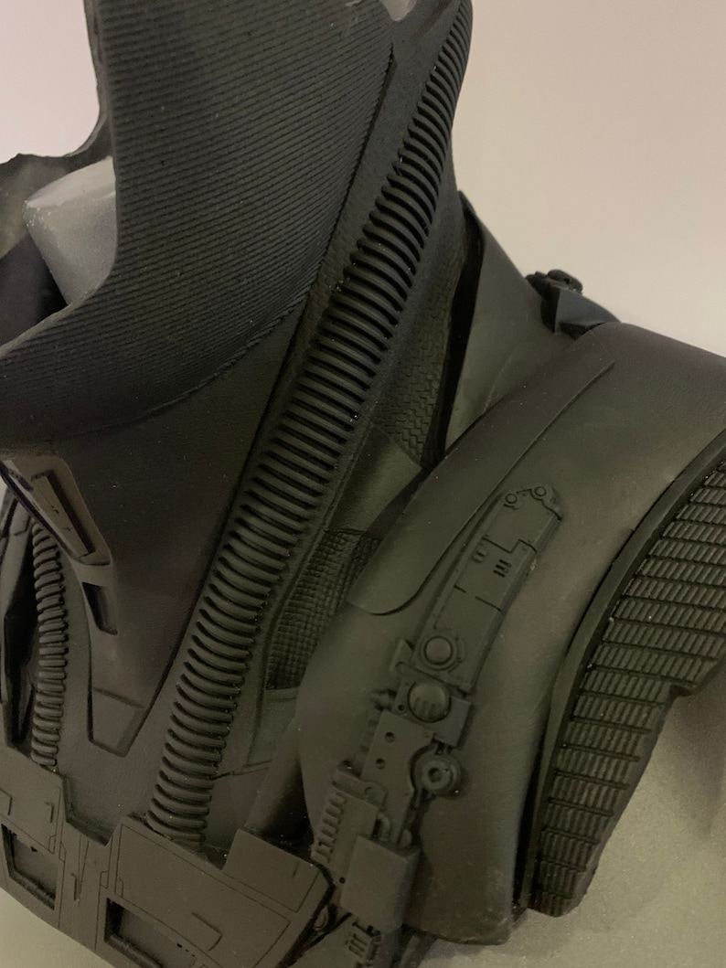 May include: A close-up of a black sculpture, possibly a bust or part of a costume. The piece has a textured, ribbed neck and shoulder area, with intricate mechanical details and a matte finish. The overall design suggests a futuristic or sci-fi theme.