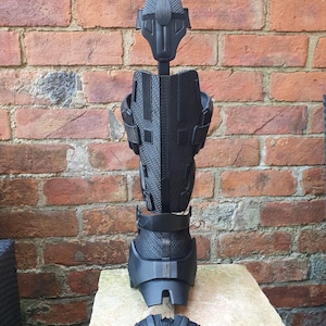 May include: A black prosthetic leg with multiple parts, including a foot, calf, shin, and knee. The leg is disassembled and laid out on a light-colored surface.