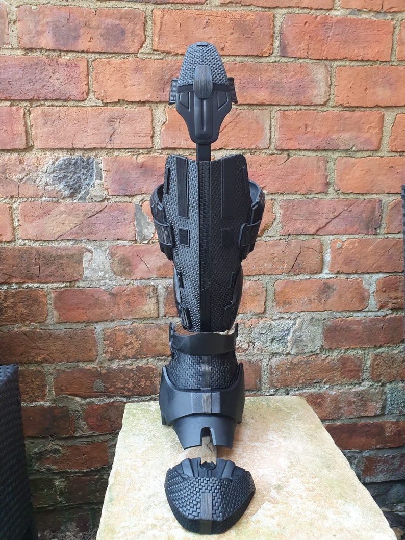 May include: A black prosthetic leg with multiple parts, including a foot, calf, shin, and knee. The leg is disassembled and laid out on a light-colored surface.