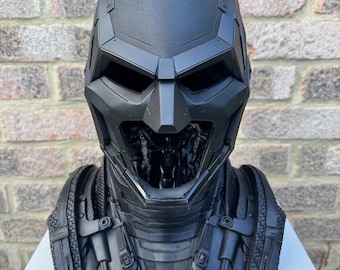May include: A matte black, three-dimensional bust of a stylized helmeted character featuring sharp, angular geometric lines, a pointed cowl, and intricate mechanical detailing across the neck and shoulder armor pieces, presented in a front-facing view.