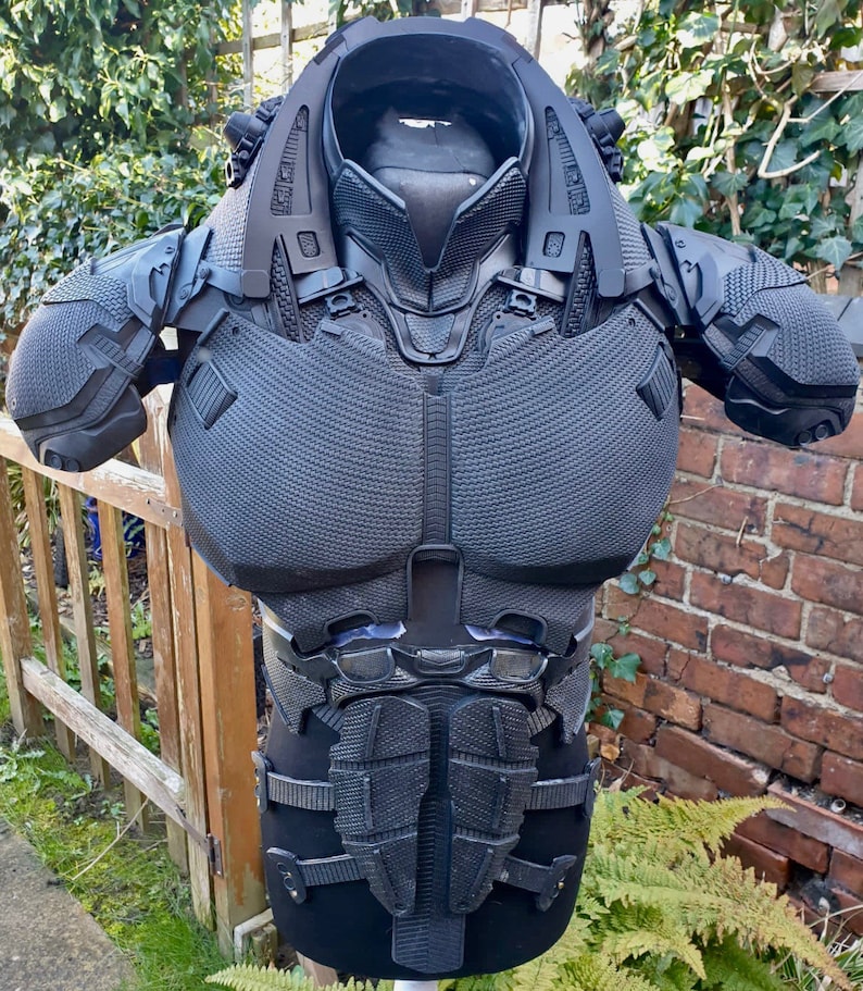 May include: Black and grey 3D printed body armour with a textured surface. The armour has a neck piece, shoulder pads, and a chest piece.