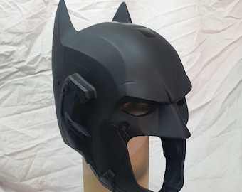 May include: A black plastic Batman helmet with a detailed design. The helmet has a raised brow, a pointed chin, and a large, open mouth.