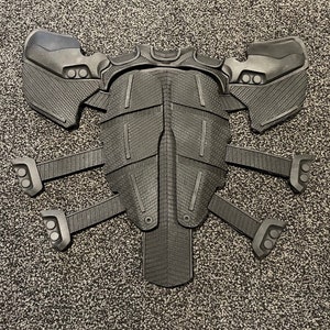 May include: Black plastic costume armour with a segmented design and multiple points. The armour has a textured surface and is shaped like a torso with arms and legs.