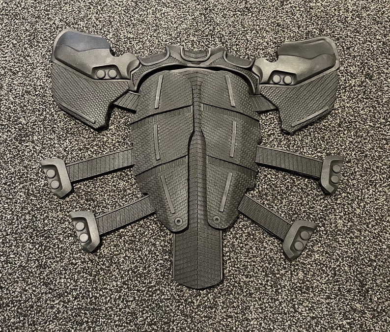 May include: Black plastic costume armour with a segmented design and multiple points. The armour has a textured surface and is shaped like a torso with arms and legs.