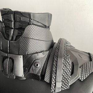 May include: Black and gray 3D printed costume piece with a textured surface and intricate details. The piece has a collar and shoulder armor design.